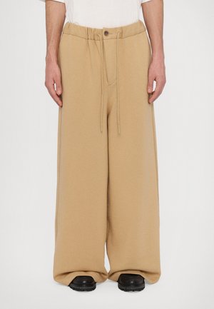 Beige wide-leg sweatpants with a drawstring waistband, featuring a soft texture and a front pocket, paired with black footwear.