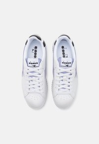 Baskets blanches avec des accents violets et noirs. Fabriquées en cuir, présentant des détails perforés et une semelle texturée. Design à lacets.