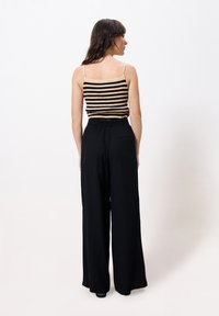 Gestreepte zwarte en beige tanktop met dunne spaghettibandjes, gecombineerd met losse zwarte broek met elastische tailleband en zijzak.