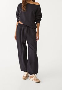 Ciemnoszara bluza z opuszczanymi ramionami i długimi rękawami, zestawiona z dopasowanymi szerokimi dresami z elastycznym pasem i bocznymi kieszeniami.