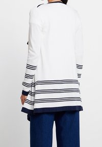 Biały kardigan z długim rękawem w granatowe paski na dole i mankietach, charakteryzujący się luźnym krojem i lekko rozszerzanym fasonem.