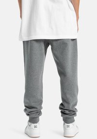 Graue Sweatpants aus einem weichen, strukturierten Stoff, mit einer entspannten Passform und schmal zulaufenden Knöcheln, kombiniert mit weißen Sneakers.