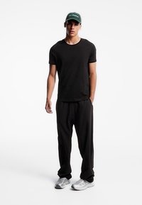 Tricou negru din bumbac, pantaloni negri largi și teniși gri, asortați cu o șapcă verde cu text alb ce spune "no drama".