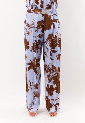 Pantaloni ampi azzurri chiaro con grande stampa floreale marrone scuro indossati con sandali crema con punta aperta.