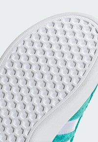 Bílá gumová podrážka boty s vzorem včelí plástve, vybavená texturovanými hexagonálními úchopy. Okraj přechází do tyrkysového vršku s bílými akcenty.