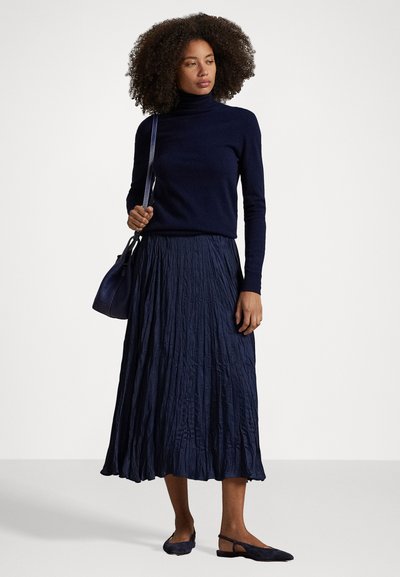 Suéter de gola alta azul-marinho, saia plissada azul-marinho e sapatilhas azul-marinho. O conjunto apresenta um design texturizado e fluido com uma silhueta casual.