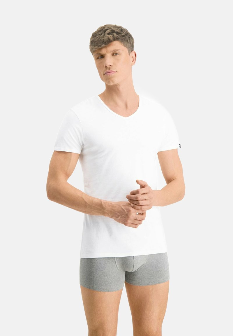 Weißes V-Ausschnitt-T-Shirt aus Baumwolle mit kurzen Ärmeln und glatter Textur. Kombiniert mit grauen Boxershorts.