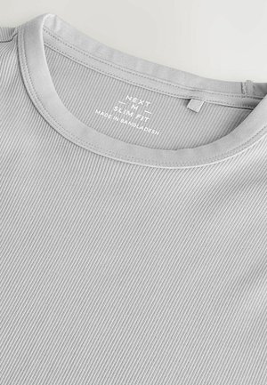Light gray ribbed t-shirt with a round neckline, featuring a label detailing "NEXT Slim Fit," made in Bangladesh. Soft fabric texture.