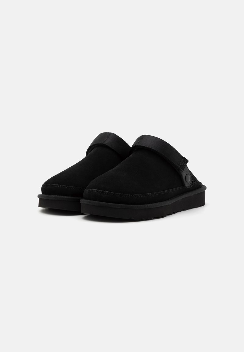 Zoccoli in suede neri con punta arrotondata e una fascia nera sopra il collo del piede. Superficie texturizzata e suola in gomma nera imbottita.