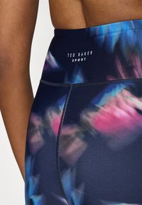 Sötétkék, magas derékú sportleggings, színes absztrakt mintázattal, varrott varratokkal és 'Ted Baker Sport' márkanevével.