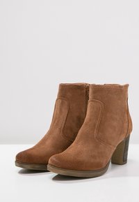 Bruine suède enkellaarsjes met een ronde neus, zijklep en een stapelhak. Gelaagd oppervlak met gestikte details.