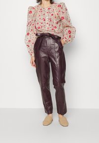 Transparente Bluse mit floralem Muster und Puffärmeln, Knopfdetails; bordeauxfarbene Lederhose mit hohem Bund; beigefarbene, gewebte Slipper.