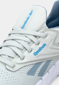 Világosszürke sportcipő, légáteresztő hálós felsőrésszel, texturált fűzőkkel, kék logóval és kiemelő csíkokkal; párnázott talp különleges mintával.
