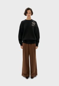 Zwarte oversized sweatshirt met een bloemenpatroon op de borst, gecombineerd met bruine wijde broek. Soepele textuur en casual pasvorm.