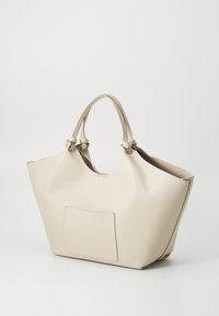 Beige lærveske med teksturert overflate, brei åpning, doble hender og en utvendig lomme. Rund form, minimalistisk design.