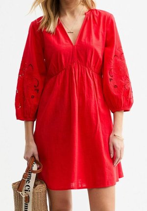 Woman wearing a red dress with embroidered balloon sleeves, holding a wicker handbag with leather straps and a printed fabric handle.
