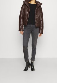 Brun puffjacka med hög krage, svart åtsittande tröja, grå slim jeans och svarta ankelstövlar med spetsiga tår.