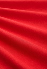 Tissu en coton rouge avec une texture lisse, présentant des plis doux et une couleur uniforme. Aucun motif visible ni accents supplémentaires.