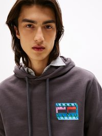 Hanorac gri cu glugă și șnururi, având o etichetă cu logo-ul multicolor "TOMMY JEANS" pe pieptul stâng. Material moale cu o textură netedă.