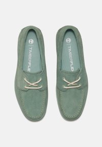 Mocassini in suede verde con lacci beige, soletta imbottita e dettagli di cucitura a contrasto. Logo Timberland visibile sulle solette.