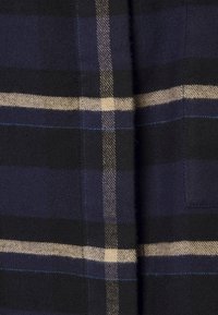 Tessuto a quadri blu navy e nero con linee beige, texture tessuta e dettagli di cucitura blu, dalla finitura liscia e leggermente lucida.
