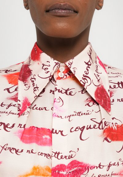 Collared shirt in lightweight fabric featuring a pattern of red and orange kiss marks with handwritten text on a cream background.