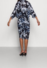 Klänning med blommönster i nyanser av marinblått och ljusblått. Har lösa ärmar och en figurnära silhuett, tillverkad av lätt tyg.