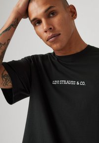 Svart bomull T-skjorte med hvit "LEVI STRAUSS & CO." logo på brystet. Korte ermer og rund hals. Myk, glatt tekstur.