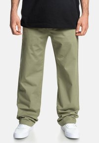 Khaki bomuldsbukser med en afslappet pasform, der har lige ben og sidelommer, parret med hvide sneakers.