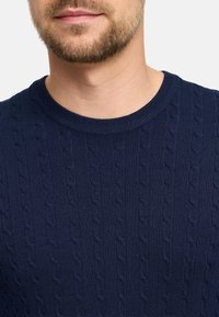 Granatowy sweter dzianinowy z teksturowanym wzorem w warkocze, okrągłym dekoltem i ściągaczami. Materiał wydaje się być miękki i trwały.
