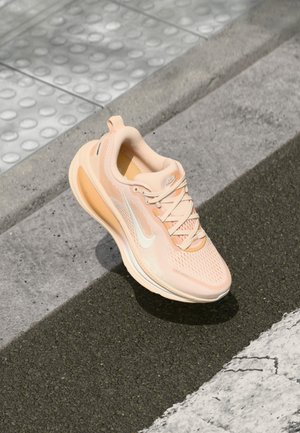 Světlé broskvové běžecké boty s prodyšným síťovaným svrškem, bílým logem swoosh, texturovanými detaily a odpruženou podrážkou.