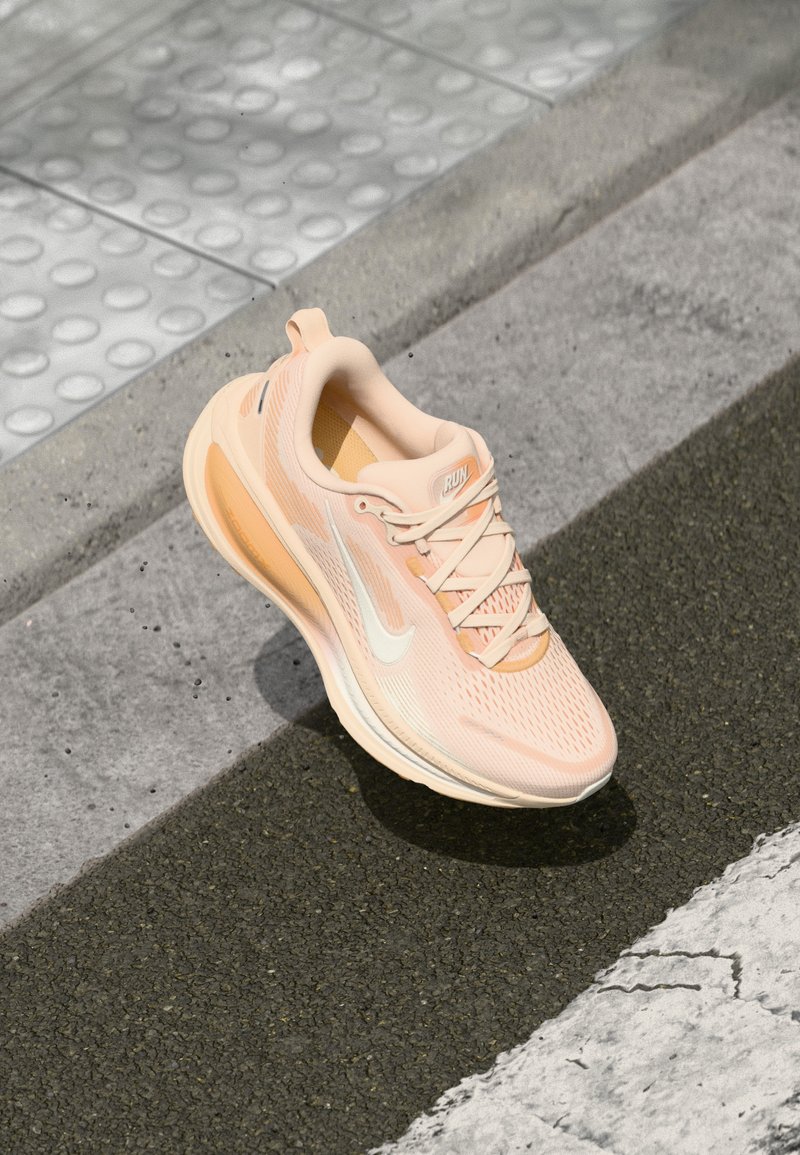 Chaussure de course légère en pêche avec une tige en maille respirante, logo swoosh blanc, détails texturés et semelle rembourrée.