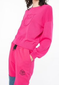 Rosa sweatshirt med upphöjt logotyp, långa ärmar och ribbade muddar, i kombination med matchande sweatpants med svart dragsko och logodetalj.