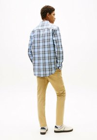 Blåternet skjorte med knaplukning og lange ærmer, beige chinos og hvide sneakers. Skjorten har krave og en afrundet kant.