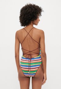 Häkel-Badeanzug mit horizontalen Streifen in mehreren Farben. Er hat einen tiefen Rücken mit gekreuzten Trägern und einem Bindedetail an der Taille.