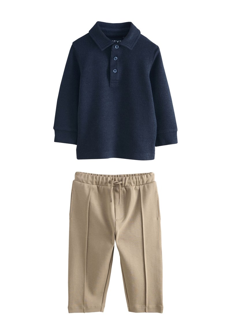 Polo bleu marine à manches longues avec trois boutons, associé à un pantalon beige à taille élastique doté de poches latérales et d'une coupe décontractée.