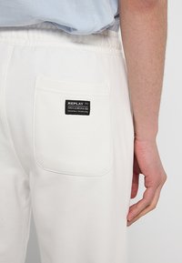Witte katoenen broek met een gestructureerde afwerking, voorzien van een elastische tailleband en een achterzak met een zwart "REPLAY" label.