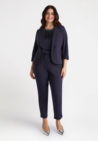 Granatowy blazer z podwiniętymi rękawami 3/4, gładka tkanina; w zestawie z granatowymi spodniami woskowymi; srebrne szpilki; prosty okrągły dekolt.