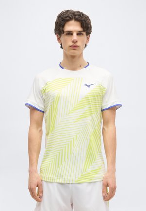 Νεαρός άνδρας που φοράει λευκό αθλητικό μπλουζάκι με γεωμετρικά μοτίβα σε νέον κίτρινο και μπλε περιμετρική λεπτομέρεια, στέκεται μπροστά σε ένα απλό φόντο.