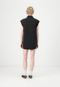 Zwart denim jurk met korte mouwen, afgeronde zoom en zichtbare stiksels. Gecombineerd met slip-on schoenen met luipaardprint en witte sokken.