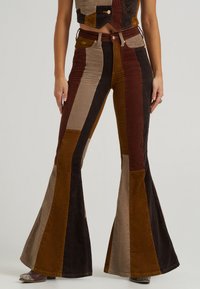 Corduroy flared pants with vertical color blocks in brown, tan, and rust. Features a high waist and a classic five-pocket design.