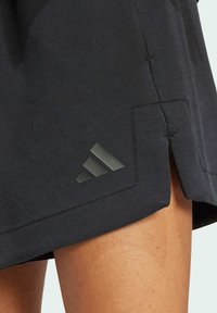 Čierna športová sukňa so bočným rozparkom, s textúrovaným logom Adidas v tmavošedej farbe blízko lemu a hladkým zložením látky.