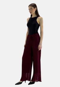 Top senza maniche nero aderente abbinato a pantaloni ampi plissettati color bordeaux, con vita elastica e una texture fluida. Scarpe nere.
