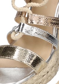 Sandalia cuña con tiras en metalizado plata y dorado con patrón de serpiente, detalle de cuerda trenzada en beige y plantilla smooth en beige.