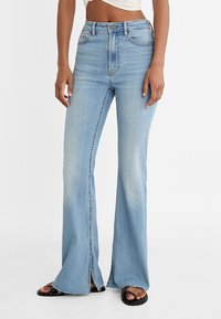 Lichtblauwe flare jeans van denim, met een hoge taille, een onafgewerkte zoom en zijslits. Gecombineerd met zwarte sandalen voor een casual uitstraling.