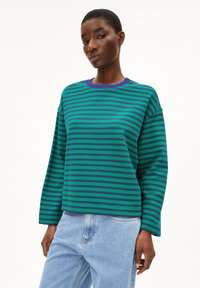 Grün und lila gestreifter Sweatshirt mit langen Ärmeln und Rundhalsausschnitt, kombiniert mit hellblauen Jeans. Der Stoff wirkt weich und lässig.