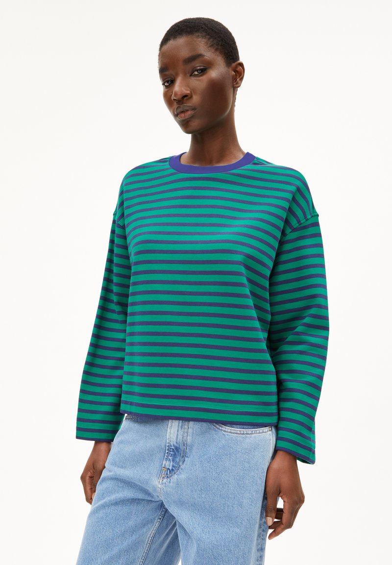 Grün und lila gestreifter Sweatshirt mit langen Ärmeln und Rundhalsausschnitt, kombiniert mit hellblauen Jeans. Der Stoff wirkt weich und lässig.