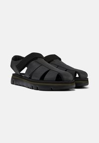 Black leather sandals with open toe design, featuring horizontal straps and elastic bands. Textured rubber sole for enhanced grip and comfort.