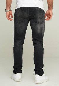 Vaqueros de mezclilla negros de corte slim, con dos bolsillos traseros y sutiles acentos metálicos. Combinados con zapatillas blancas.