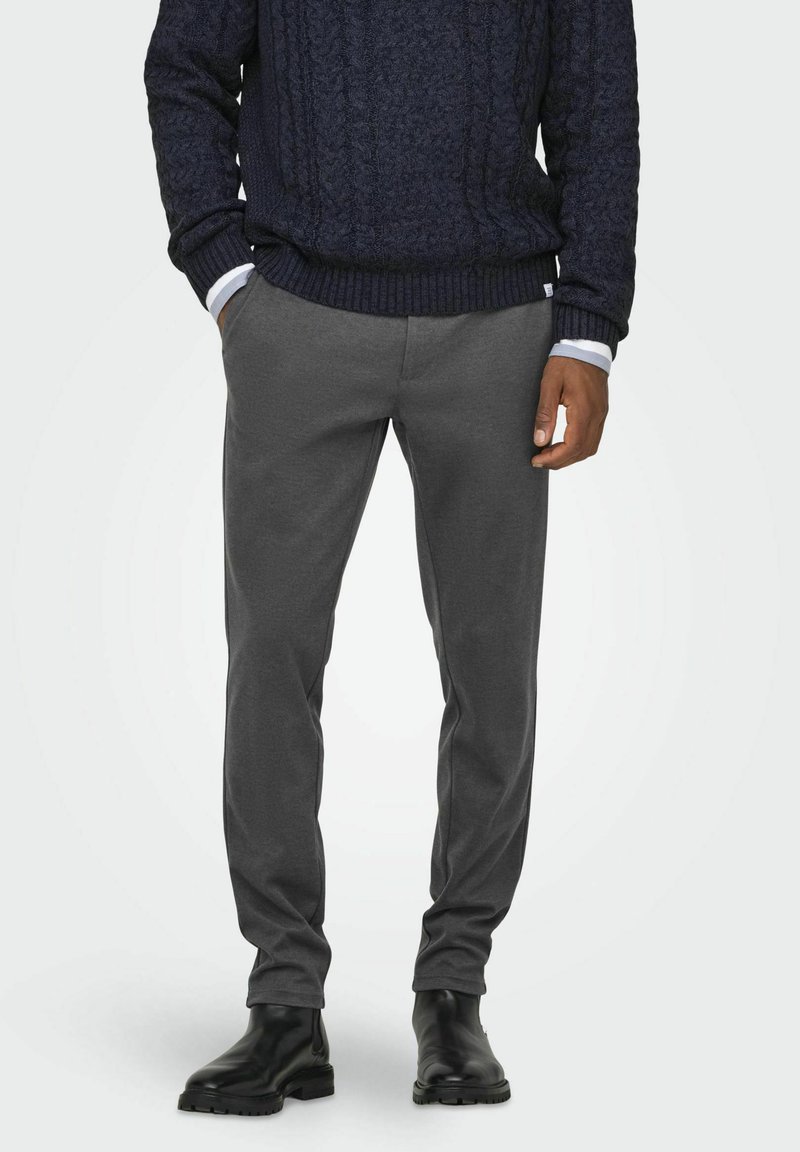 Pull en maille torsadée marine avec des poignets côtelés, associé à un pantalon gris fuselé et des bottines noires. Présente un tissu doux et une silhouette près du corps.